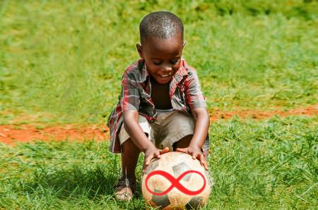 Niño cogiendo un balón de fútbol muy feliz. En el balón hay un símbolo del infinito.